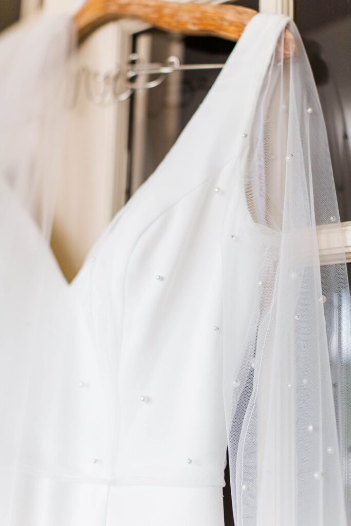 Close up of the brides white wedding dress with pearls attached to the sleeve of the dress
