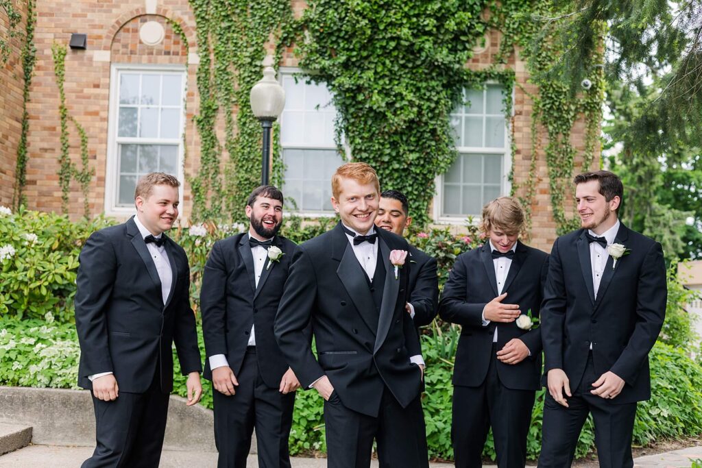 Groomsmen in black tuxedos laugh and cheer the groom on as her smiles towards the camera of a Coeur d'Alene Wedding photographer 