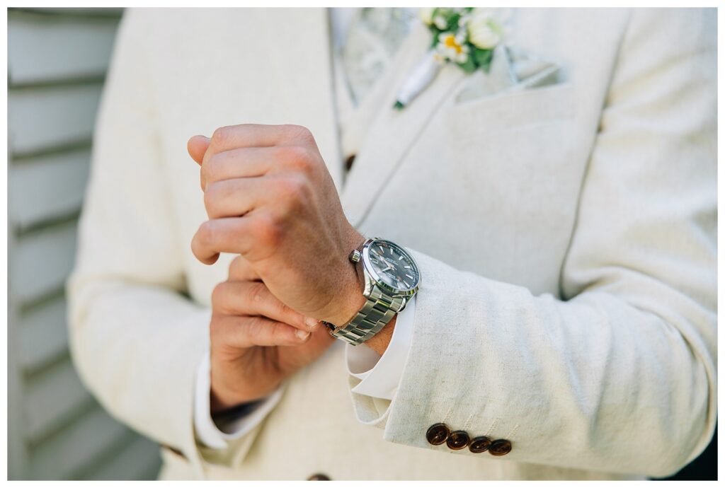 Groom in linen cream suit adjusting his silver watch for his Groom wedding photos 