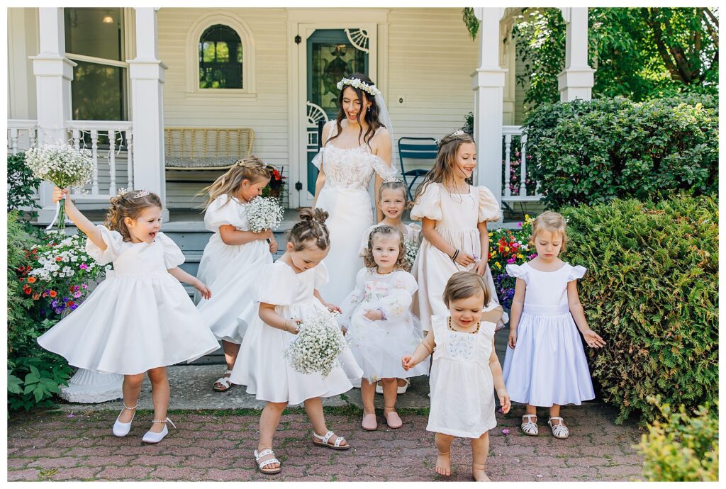 Bride twirling in front of the Belle gardens venue with her eight flower girls in satin dresses holding bouquets of baby's breath  