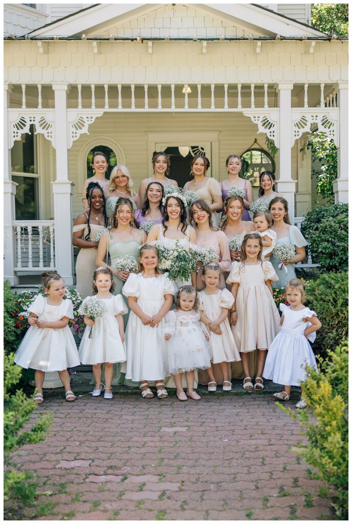 Bride with her bridesmaids in pastel spring colors line up for a wedding photo in front of the belle gardens wedding venue cottage 