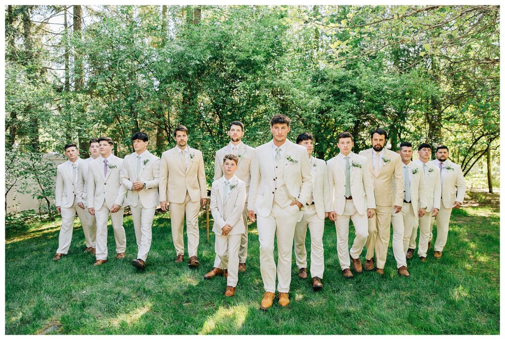 Groom and groomsmen with cream suits and pastel ties walking for their groomsmen wedding photos