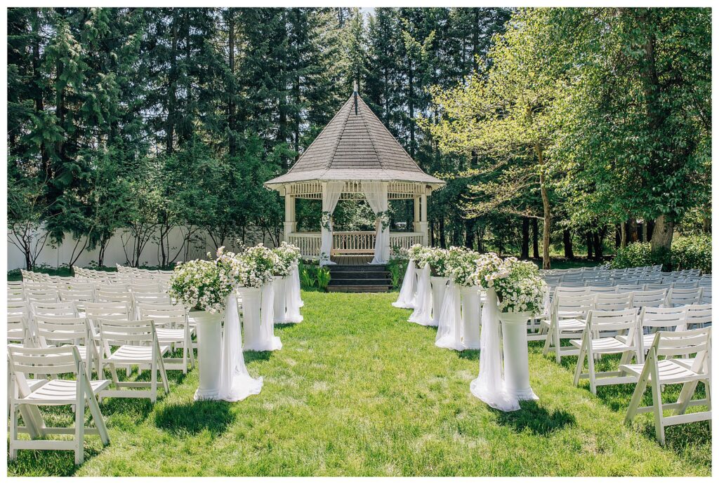 The view of the ceremony setup at Belle gardens with white pillars lining the aisle with trailing white flowers on each pillar with the gazebo as the central focus