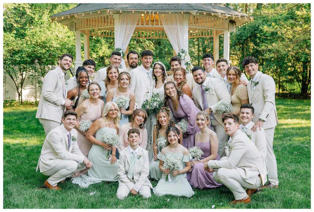 Bridal party in spring pastel colored chiffon dresses and groomsmen in cream linen suits smile with the bride and groom 